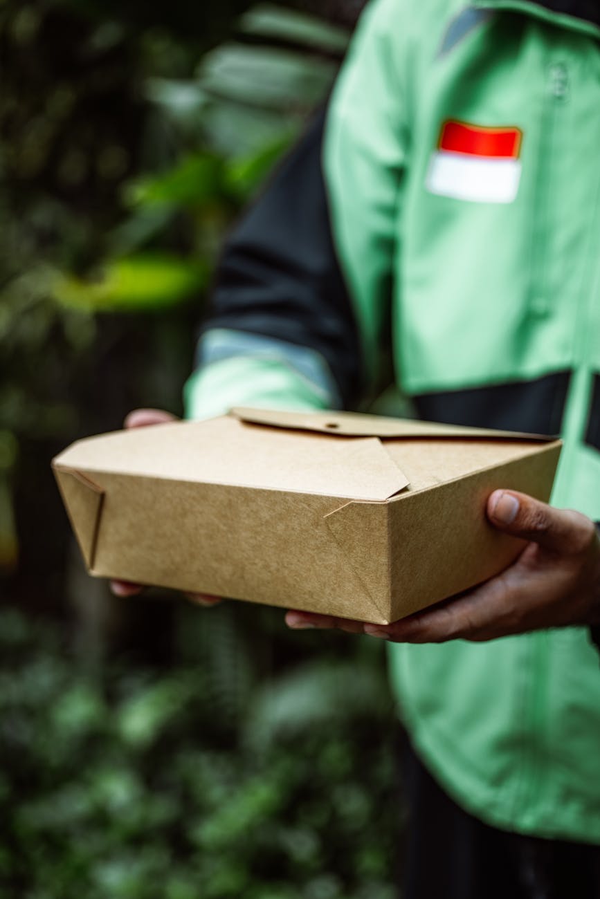 Close-up of a person holding a biodegradable food delivery box outdoors.